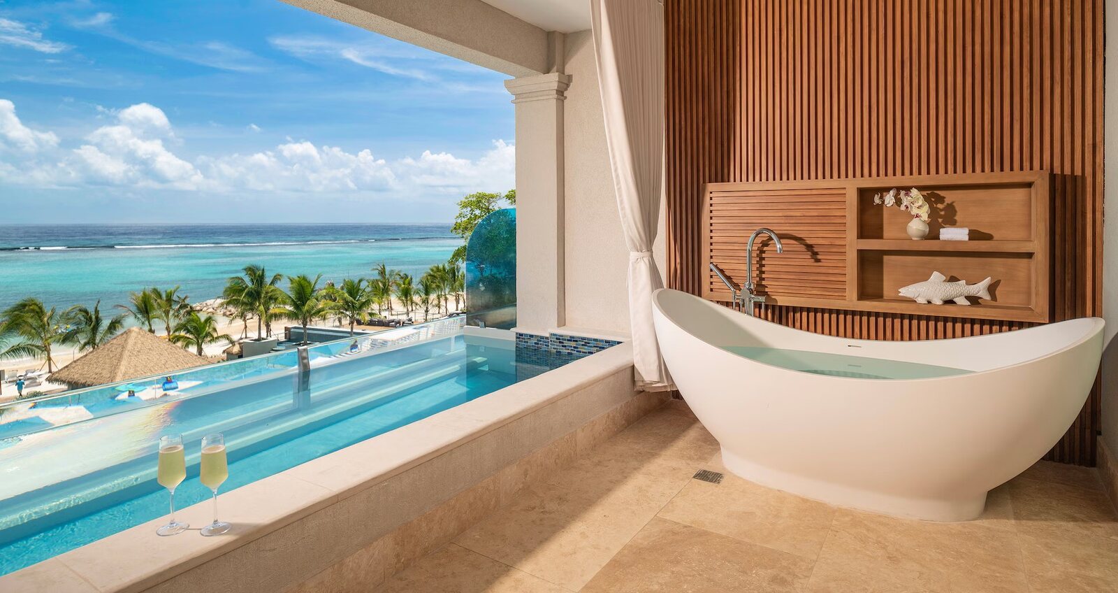 Two glasses of champagne on a private plunge pool beside a soaking tub on a Sandals honeymoon