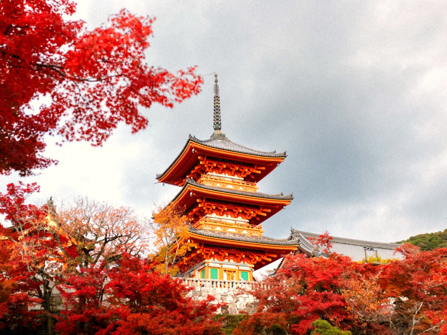 Three-story pagoda at Kiyomizu-dera framed by red autumn maples in Kyoto, Japan
